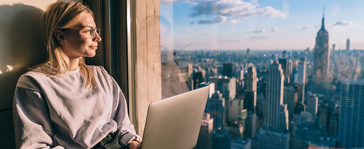 A businesswoman looks out over the NYC skyline from a hotel room