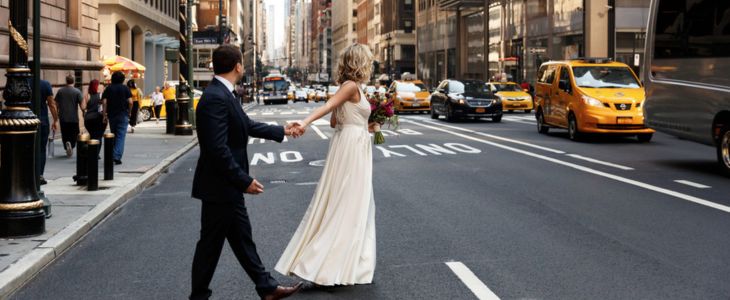 a bride and groom hold hands crossing a busy nyc street
