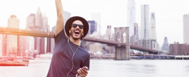 a man listening to music smiles and cheers in front of the new york city skyline