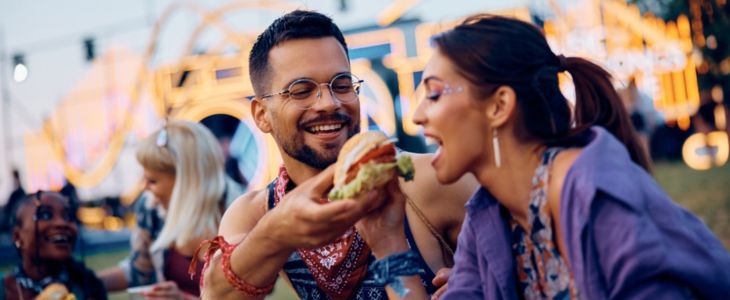 a woman takes a bite of a sandwich at a festival