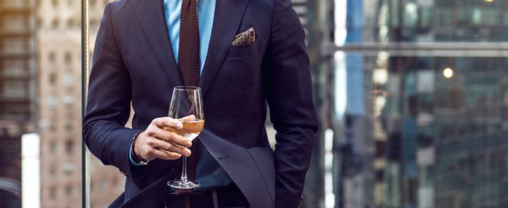 a gentleman in a suit holds a glass of wine at a rooftop bar in new york city